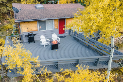 A cozy cabin with a red door and a spacious deck surrounded by vibrant autumn foliage.