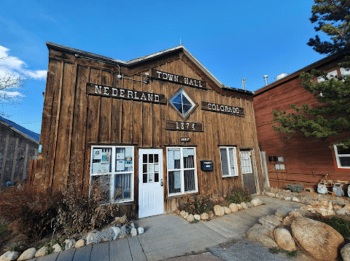 Historic wooden building of Nederland Town Hall, Colorado, with a sign displaying "1874" and a clear blue sky.