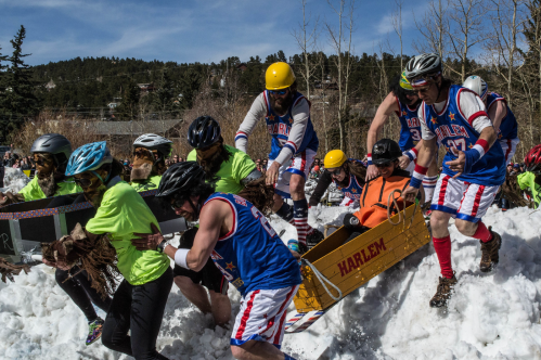 A group of people in colorful outfits and helmets push a sled through snow during a fun winter event.