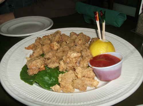 A plate of fried chicken bites on lettuce, served with a lemon wedge and a side of dipping sauce.