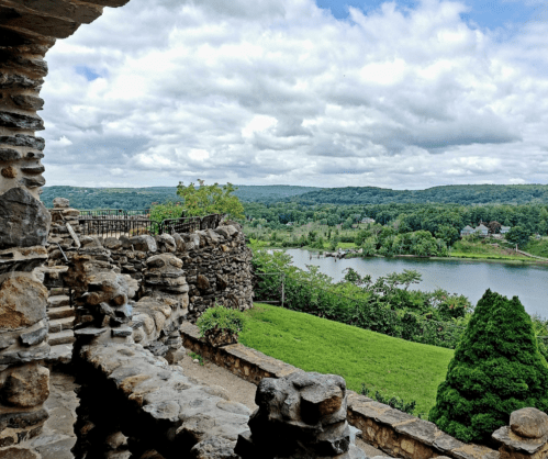 Scenic view from a stone structure overlooking a river and lush green landscape under a cloudy sky.