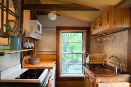 Cozy kitchen with wooden cabinets, a sink, stove, and a window overlooking greenery. Bright and inviting atmosphere.