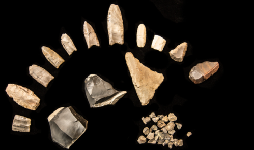 A collection of various stone tools and flakes arranged on a black background.