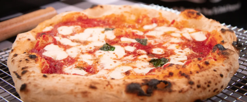 A freshly baked pizza with melted mozzarella, tomato sauce, and basil on a cooling rack.