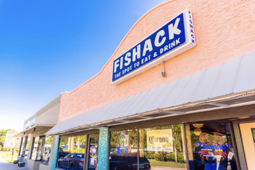 Exterior of a restaurant named "Fishack," featuring a colorful sign and large windows, under a clear blue sky.