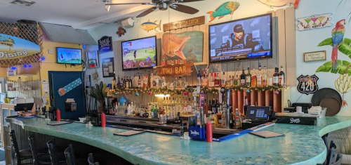 A vibrant tiki bar with a curved counter, colorful decor, and multiple TVs displaying sports events.