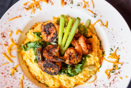 A plate of creamy grits topped with seasoned shrimp, spinach, and celery, garnished with cheese and spices.