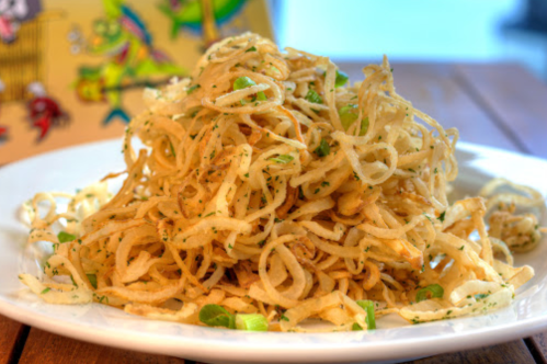 A plate of crispy, golden-brown fried noodles garnished with green herbs, served on a wooden table.