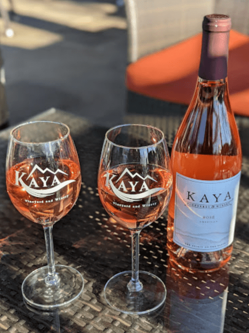 Two glasses of rosé wine with a bottle, all branded with "KAYA," set on a textured table.