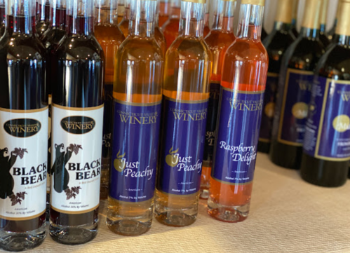 Bottles of various fruit wines displayed on a table, including Black Bear, Just Peachy, and Raspberry Delight.