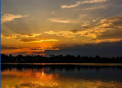 A serene sunset over a calm lake, with vibrant orange and yellow hues reflecting on the water's surface.