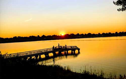 A serene sunset over a lake, with a wooden pier and silhouettes of people enjoying the view.