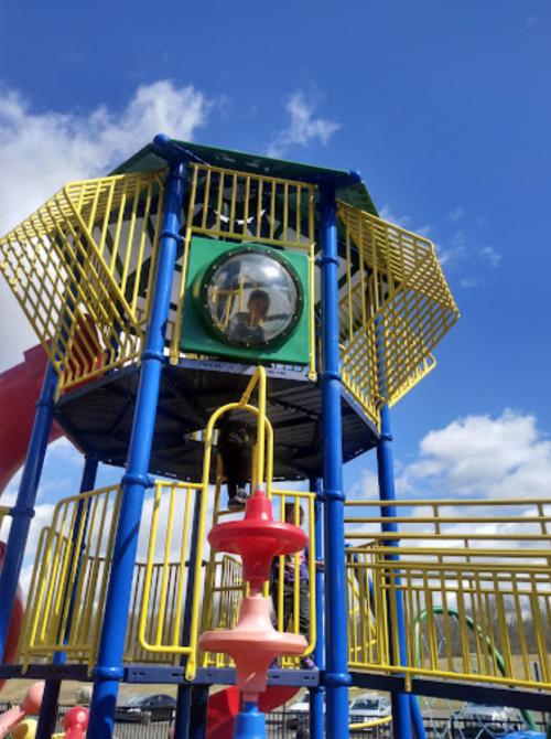 A colorful playground structure with a slide and a child peering through a round window on a sunny day.