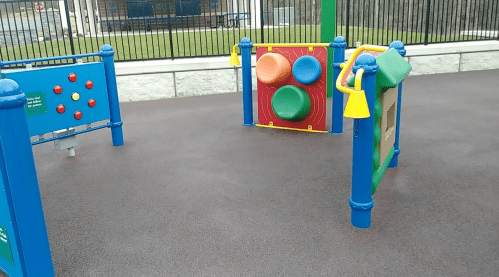 Colorful playground equipment with interactive panels and sensory features on a rubber surface.