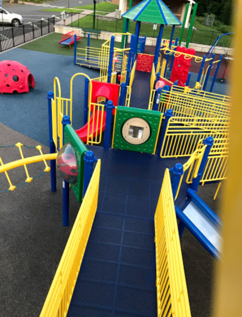 Colorful playground with slides, climbing structures, and a circular window, surrounded by safety barriers.