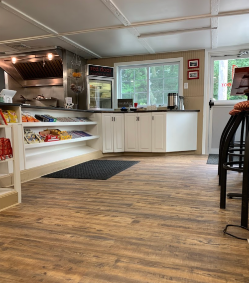 A cozy shop interior with wooden floors, shelves of snacks, and a counter near a window.
