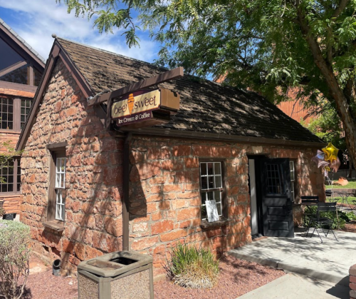 A small stone building with a sign reading "beesweet" and outdoor seating, surrounded by greenery.