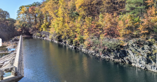 A serene river surrounded by vibrant autumn foliage and rocky banks under a clear blue sky.