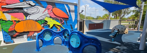 Colorful playground with blue equipment and a vibrant mural of animals on the wall in a sunny outdoor setting.