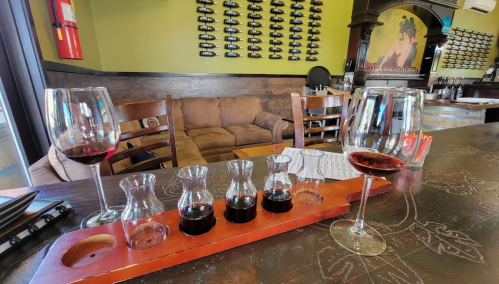 A cozy wine bar with a tasting flight of red wines and two glasses on the counter, featuring a comfortable seating area.