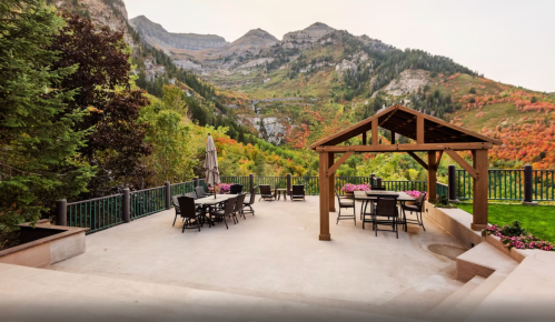 Scenic outdoor patio with seating, surrounded by lush greenery and mountains in the background.