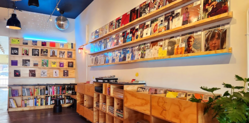 A cozy record store with wooden shelves displaying vinyl records and books, featuring colorful lighting and a disco ball.