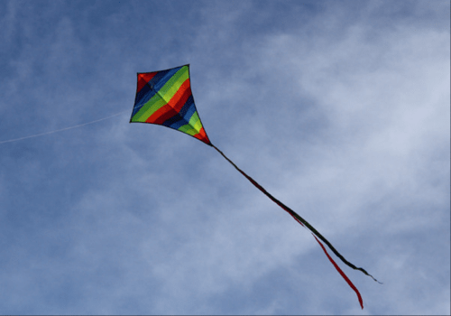 A colorful rainbow kite soaring against a blue sky with wispy clouds.
