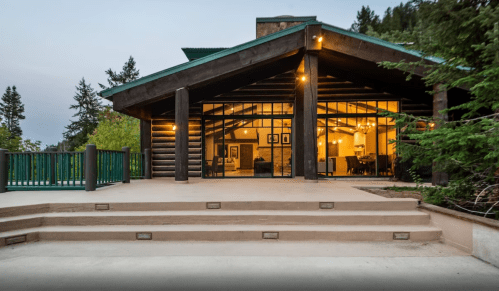 Modern cabin with large windows, wooden beams, and a spacious patio surrounded by trees.
