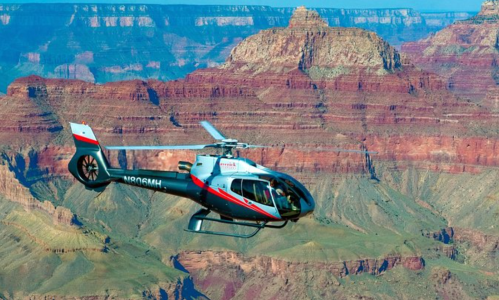 A helicopter flies over the Grand Canyon, showcasing the colorful rock formations and vast landscape below.