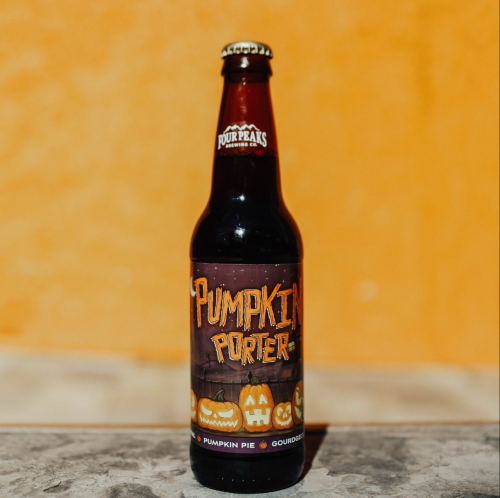A bottle of Pumpkin Porter beer with a festive label featuring pumpkins and a Halloween theme against an orange background.
