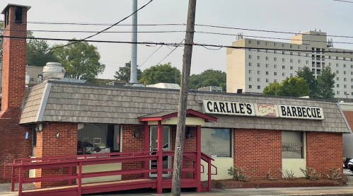 A brick barbecue restaurant with a sloped roof and a red ramp, surrounded by trees and buildings in the background.