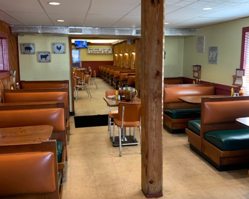 Interior of a diner featuring booths, tables, and a wooden pillar, with warm lighting and a cozy atmosphere.