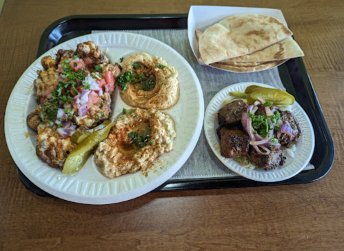 A plate of hummus, grilled meat, pita bread, and garnished vegetables on a tray.