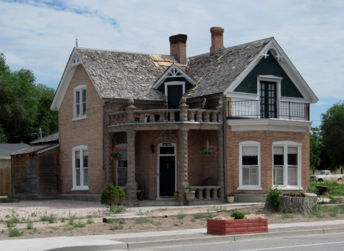 A historic two-story brick house with a unique balcony, decorative trim, and a landscaped front yard.