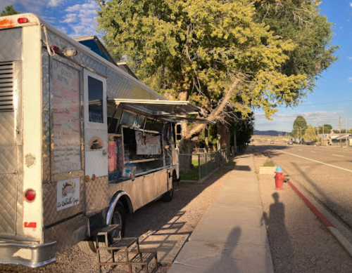 A food truck parked by the roadside, with a tree nearby and a clear blue sky in the background.
