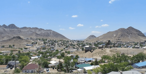 A panoramic view of a small town surrounded by mountains under a clear blue sky.
