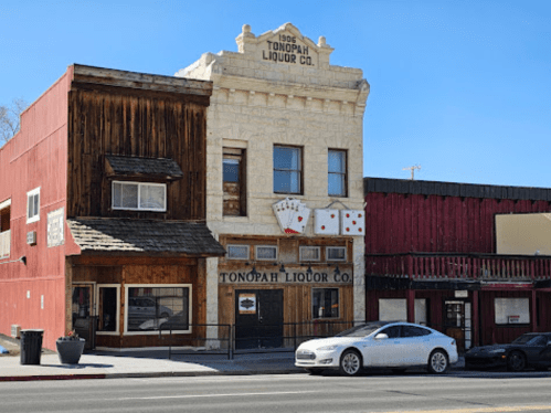 Historic Tonopah Liquor Co. building with a stone facade and playing cards on display, alongside a red wooden structure.