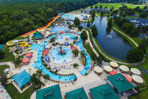 Aerial view of a water park featuring slides, pools, and a lazy river, surrounded by greenery and a pond.