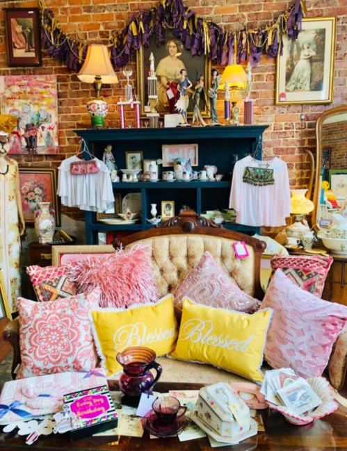 A cozy vintage display featuring decorative pillows, antiques, and a brick wall backdrop with various collectibles.