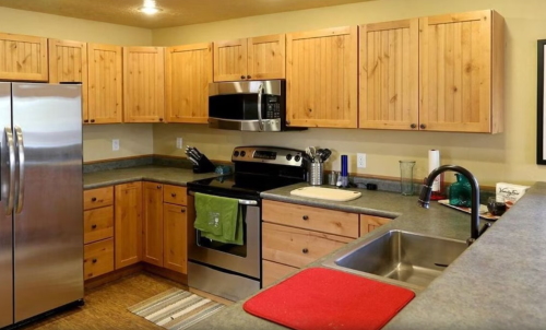 A modern kitchen with wooden cabinets, stainless steel appliances, and a countertop with a sink and cutting board.