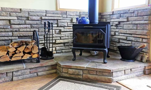 A cozy corner featuring a black wood stove, stacked firewood, and stone walls, creating a warm atmosphere.