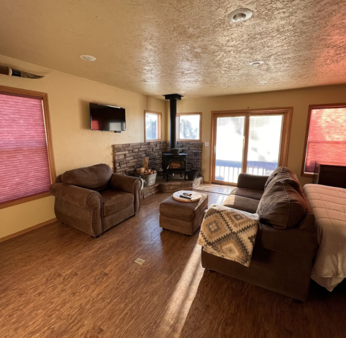 Cozy living room with brown furniture, a stone fireplace, and large windows with red shades.