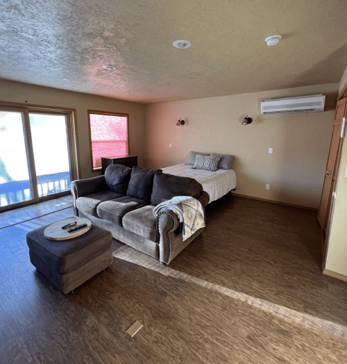 Cozy living space featuring a sofa, ottoman, bed, and large windows with natural light.