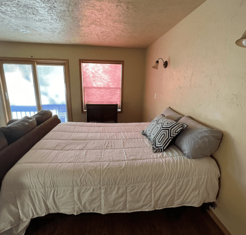 Cozy bedroom with a bed, decorative pillows, and large windows letting in natural light.