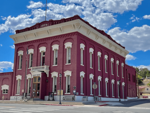 Historic red brick courthouse with white trim, built in 1879, under a blue sky with fluffy clouds.