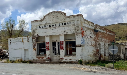 Abandoned general store with peeling paint and weathered signage, set against a cloudy sky.