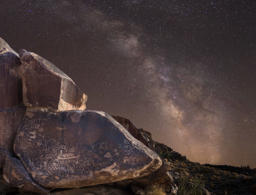 Petroglyphs on a rock under a starry sky with the Milky Way visible in the background.