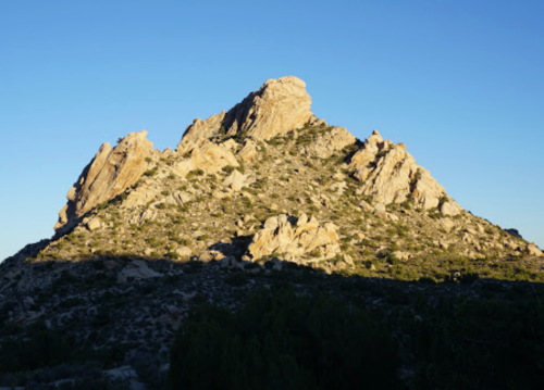 A rugged mountain peak bathed in sunlight against a clear blue sky, with shadows on the foreground.
