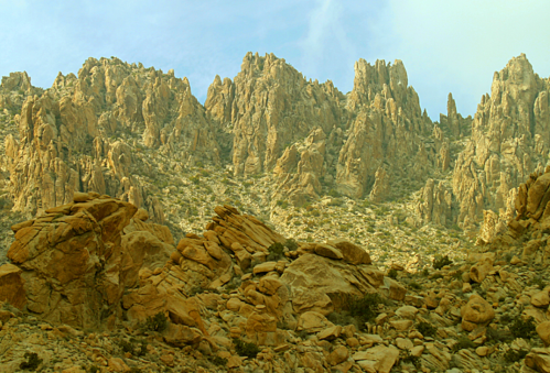 Rocky mountain landscape with rugged peaks and scattered boulders under a light blue sky.