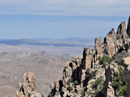 Rocky mountain landscape with rugged cliffs and distant hills under a clear blue sky.